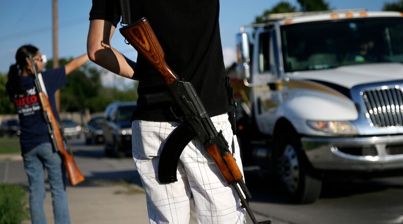 Kory Watkins, front, coordinator for Open Carry Tarrant County carries his Romanian AK 47 over his shoulder as he and his wife Janie, rear, along with others gather for a demonstration, Thursday, May 29, 2014, in Haltom City, Texas. North Texas gun rights advocates are suing the city of Arlington for amending an ordinance that they claim is discriminatory and infringes upon free speech rights, in the latest sign of growing tensions among gun activists and government forces in Texas. (AP Photo/Tony Gutierrez)