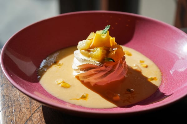 A brightly lit dessert of peach pavolova in a colorful bowl, with diced peaches on top of the dessert which is surrounded by a sauce.