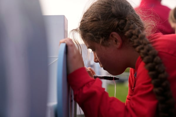 Nine-year-old Coralie Glessner writes on a heart for Alma Buhnerkempe at a vigil for three young children and a teenager, including Buhnerkempe, who were killed when a car barreled through a building used for an after-school camp Tuesday, April 29, 2025, in Chatham, Ill. (AP Photo/Erin Hooley)