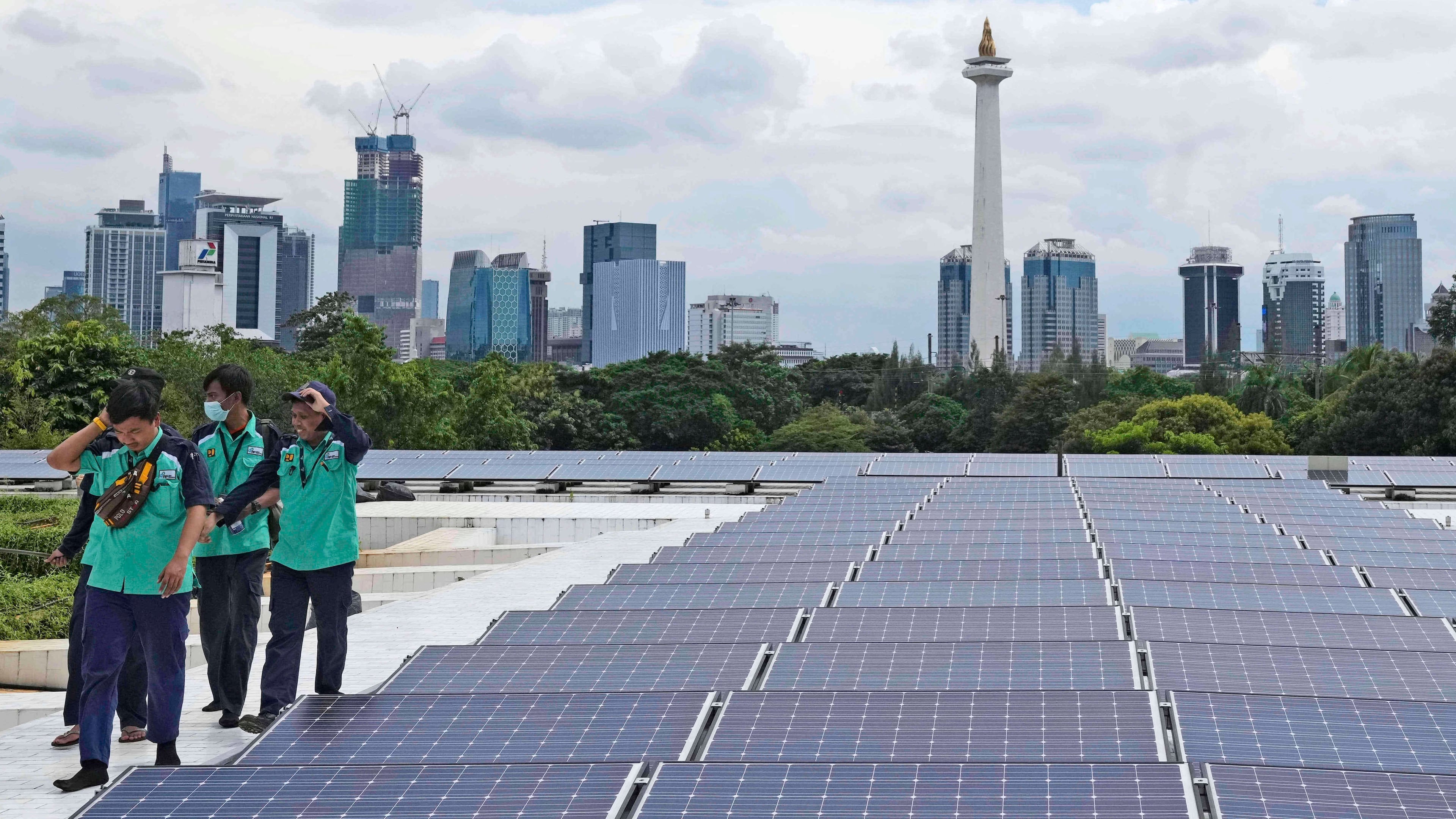 FILE - Workers walk near solar panels that provide partial electrical power to Istiqlal Mosque as the city skyline is seen in the background, in Jakarta, Indonesia, Wednesday, March 29, 2023. (AP Photo/Tatan Syuflana, File)