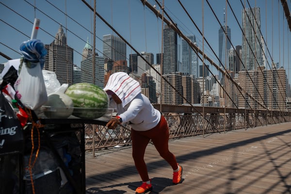 A fruit vendor pushes her cart on the Brooklyn Bridge during a heatwave on Tuesday, June 24, 2025, in New York. (AP Photo/Olga Fedorova)