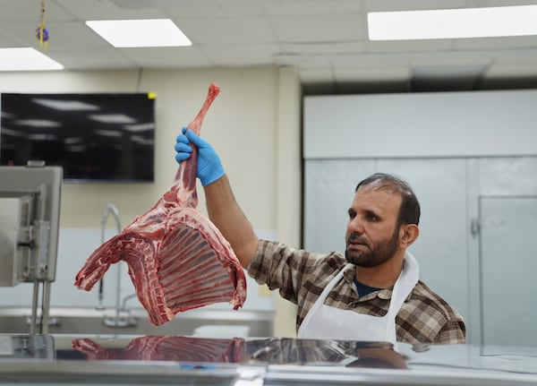 Shahpoor Essazada, a butcher at the Finest Supermarket halal grocery store in Fredericksburg, Va., holds up a piece of meat for a customer, on Monday, April 7, 2025. (AP Photo/Jessie Wardarski)