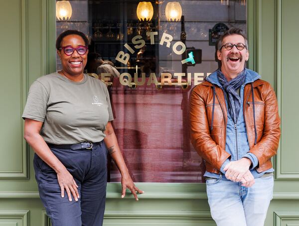 A woman, left, and a man, right, standing in front of a restaurant's plate-glass window and laughing.
