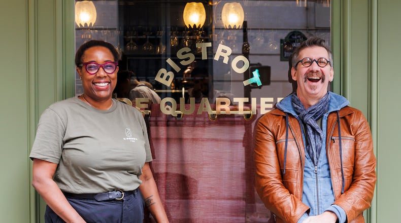 A woman, left, and a man, right, standing in front of a restaurant's plate-glass window and laughing.