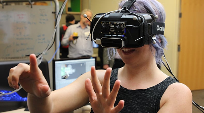 Virtual reality technology plays into expectations about our computing future. One perplexing challenge: people sometimes get nauseous trying to move with the headgear on. Here, the leader of a local VR program development company tries on a  headset at a Georgia Tech event.