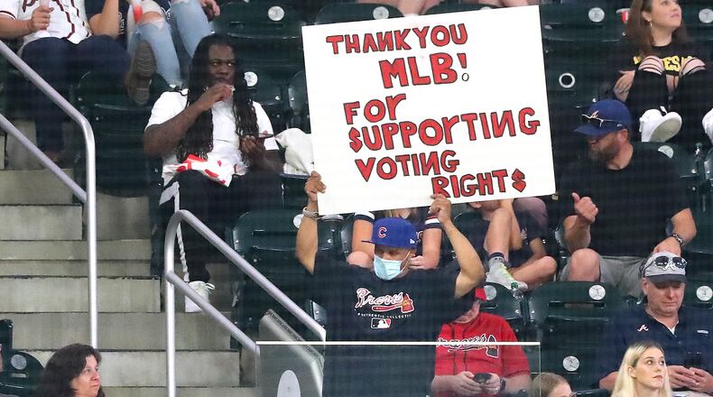 A fan - wearing a Braves jersey and a Cubs hat - holds a sign thanking Major League Baseball for "supporting voting rights" during the fifth inning of a Braves-Cubs game Monday, April 26, 2021, at Truist Park in Atlanta.  MLB moved the 2021 All-Star Game out of Atlanta over Georgia's new voting law. The July 13 game will now be played in Denver. (Curtis Compton / Curtis.Compton@ajc.com)