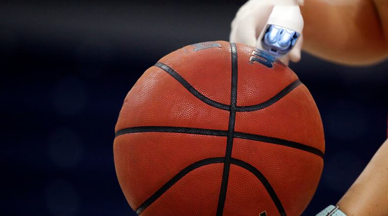 An worker waves an ultra violet lamp over the ball to kill germs during an NCAA basketball game. (Butch Dill/AP)