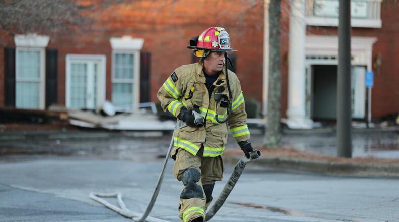 Firefighters mop up after a predawn fire destroyed a medical office building in Alpharetta. The city is seeking a federal grant to buy specialized washing machines to handle firefighters’ turnout gear. JOHN SPINK / JSPINK@AJC.COM
