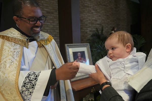 The Rev. Ricky Malebranche holds the hand of 9-month-old Andres Roman Marquez after baptizing him at St. Louis Catholic Church in Alexandria, Va., on Saturday, May 24, 2025. (AP Photo/Luis Andres Henao)