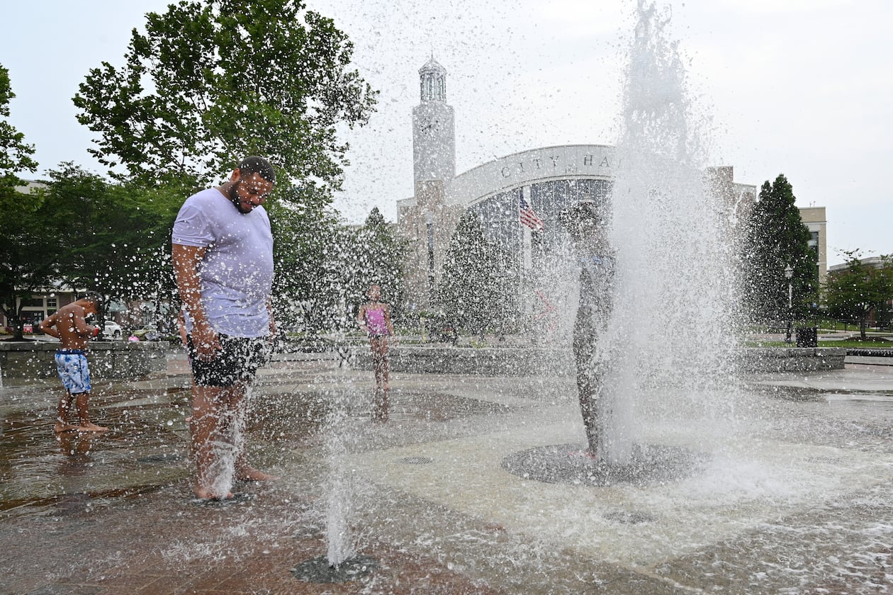 Adam Parker (left), of Suwanee, and his children play in the splash fountain at Town Center Park, Friday, June 30, 2023, in Suwanee. (Hyosub Shin/AJC)