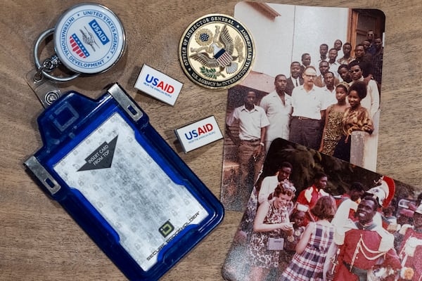 Anna Eisenberg's empty USAID badge holder is seen next to USAID pins, a coin from the USAID Office of Inspector General awarded to her mother, Cathy Votaw, and photographs of her grandfather, Albert Votaw, and his family during his service with USAID in West Africa circa 1968, Thursday, Feb. 27, 2025, in Washington. (AP Photo/Jacquelyn Martin)