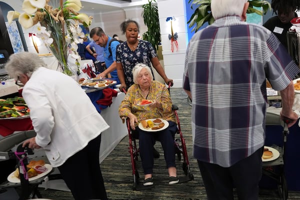 Private nursing assistant Mona Dagobert, center top, helps Eleanor Kirshner, 86, maneuver her wheelchair as she picks food from an Independence Day buffet, in the independent living community at the Toby and Leon Cooperman Sinai Residences, July 4, 2025, in Boca Raton, Fla. (AP Photo/Rebecca Blackwell)