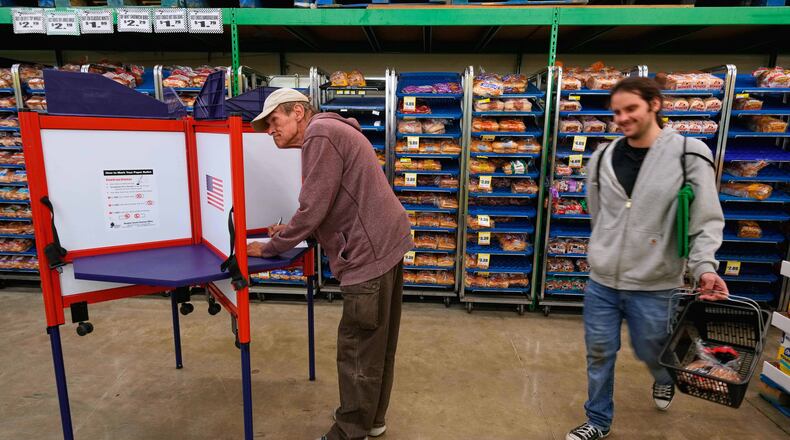Bob Walser votes while a shopper walks past at the Checkers grocery store in Lawrence, Kan., Tuesday, Nov. 4, 2025. (AP Photo/Charlie Riedel)