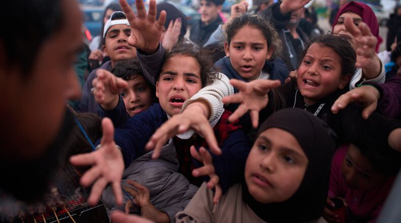 Displaced families extend their hands while waiting for donated food beside the tents they use as shelters after fleeing Israeli bombardment in southern Lebanon, in Beirut, Lebanon, Thursday, April 9, 2026. (AP Photo/Emilio Morenatti)