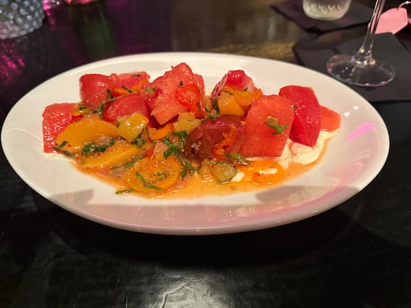 A plate filled with peaches, tomatoes and salad dressing sits on a table. The stem of a wine glass is visible in the background.