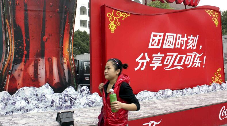 Coca-Cola Company’s chief executive said some Coke manufacturing plants in China were shuttered in the wake of the latest coronavirus, but the company is contemplating some re-openings to safely meet the population’s needs. In this 2010 photo, a woman walks past a Coke advertisement in central China’s Hubei Province. China is a major market for the Atlanta-based company.