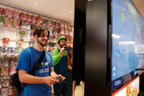 Darren Stallcup, left, of San Francisco reacts as Nicholas Oehlberg, right, of San Francisco documents the event as they play the Mario Kart World for Nintendo Switch 2 game with others at the Nintendo Store for a pre-launch event for the Ninentdo Switch 2 on Wednesday, June 4, 2025, in San Francisco. (Lea Suzuki/San Francisco Chronicle via AP)