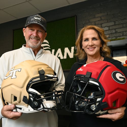 Lee and Erin Hanson, co-founders of Guardian Sports, hold Guardian Caps with Georgia Tech and UGA logos as they pose for a photo at Guardian Sports' headquarters, Tuesday, Oct. 21, 2025, in Peachtree Corners. The Guardian Cap is the leading soft shell helmet cover engineered for impact reduction. (Hyosub Shin/AJC)