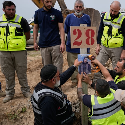 Paramedics attach a portrait over the grave of Ghadir Baalbaki, 19, who was killed on Tuesday in an Israeli airstrike, at a temporary mass grave in the southern port city of Tyre, Lebanon, Wednesday, April 15, 2026. (AP Photo/Hussein Malla)