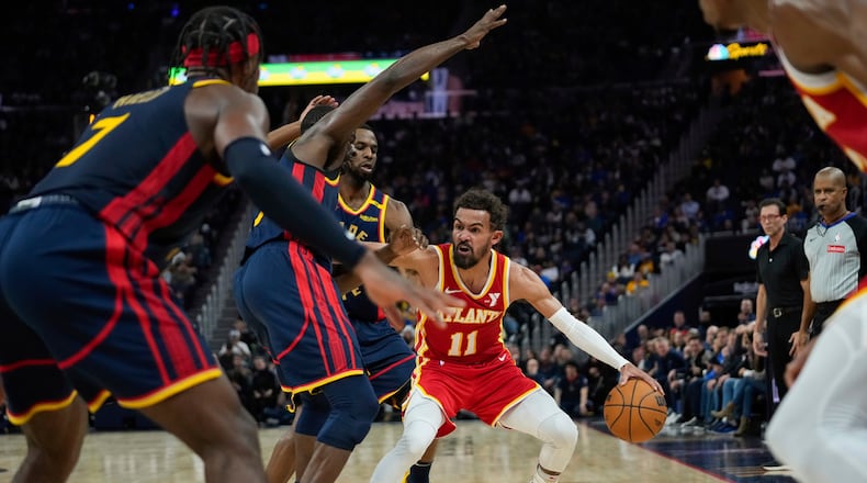 Atlanta Hawks guard Trae Young (11) looks for an open teammate while defended by Golden State Warriors forwards Draymond Green, second from left, and Andrew Wiggins during the first half of an NBA basketball game Wednesday, Nov. 20, 2024, in San Francisco. (AP Photo/Godofredo A. Vásquez)