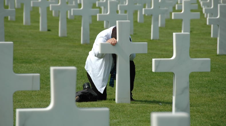 Dimitri Dodys took this picture during a visit to Normandy France in August 2017. The unidentified man was kneeling in prayer at this grave site. The Normandy American Cemetery and Memorial in France is located in Colleville-sur-Mer, on the site of the temporary American St. Laurent Cemetery, established by the U.S. First Army on June 8, 1944 as the first American cemetery on European soil in World War II. The cemetery site, at the north end of its half mile access road, covers 172.5 acres and contains the graves of 9,385 of American military dead, most of whom lost their lives in the D-Day landings and ensuing operations. On the Walls of the Missing, in a semicircular garden on the east side of the memorial, are inscribed 1,557 names. Rosettes mark the names of those since recovered and identified.