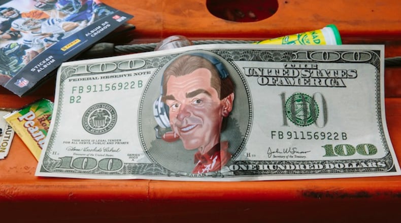 A poster of a mock $100 bill featuring a caricature of University of Alabama head football coach Nick Saban outside Bryant-Denny Stadium during homecoming weekend, in Tuscaloosa, Ala., Oct. 10, 2015. Over the past decade, the success of Alabama’s football program has become a powerful engine for the university’s economic and academic growth. (Edmund D. Fountain/The New York Times)
