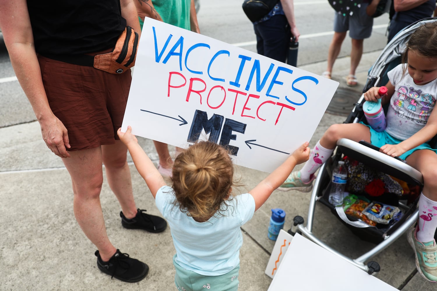 A young girl holds a sign outside of the CDC in Atlanta on Wednesday, June 25, 2025.  As Health and Human Services Secretary Robert F. Kennedy Jr. purged and reconstituted CDC vaccine advisory panel, ACIP, convenes for the first time, CDC advocates gather to protest on the dangers to health. (Abbey Cutrer / AJC)