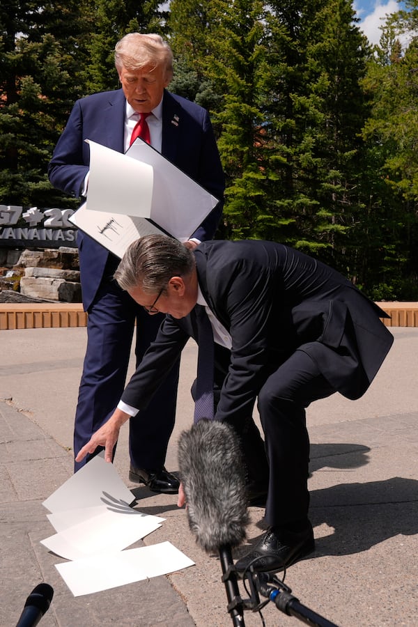 Britain's Prime Minister Keir Starmer picks up papers that President Donald Trump dropped as they meet on the sidelines of the G7 Summit, Monday, June 16, 2025, in Kananaskis, Canada. (AP Photo/Mark Schiefelbein)