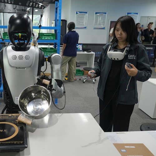 A worker remote controls humanoid robots during the one month countdown of 2026 China International Fair for Trade in Services (CIFTIS) at a robot training center in Beijing, China, Monday, Aug. 10, 2026. (AP Photo/Achmad Ibrahim)