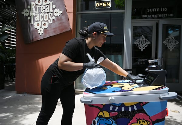 Patricia Sulbaran, staff at Rreal Tacos, places a food order inside delivery robot Darcie made by Serve Robotics. The robot was painted by Atlanta muralist George F. Baker III. (Hyosub Shin/AJC)