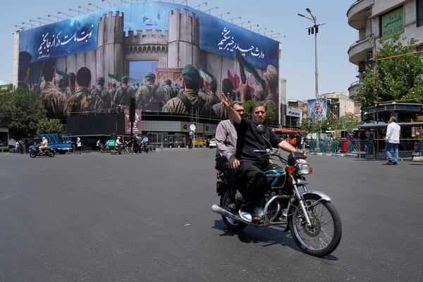 A man flashes a victory sign while riding his motorbike past an anti-Israeli banner depicting Iranian soldiers heading to attack Israeli territory, at Islamic Revolution Square in Tehran, Iran, Saturday, June 14, 2025. (AP Photo/Vahid Salemi)