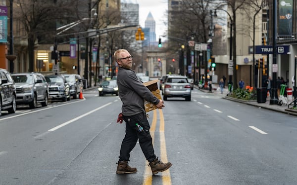A man carrying boxes jaywalks across Peachtree Street on Wednesday, Feb 11, 2026. (Ben Hendren for the AJC)