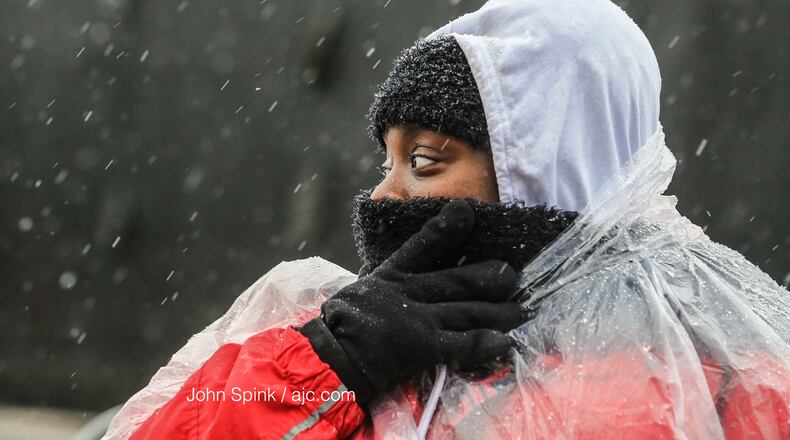 Trina Cloud, who works security, protects her face from the snow and sleet mix falling at Mercedes- Benz Stadium, where Georgia high school football is underway.