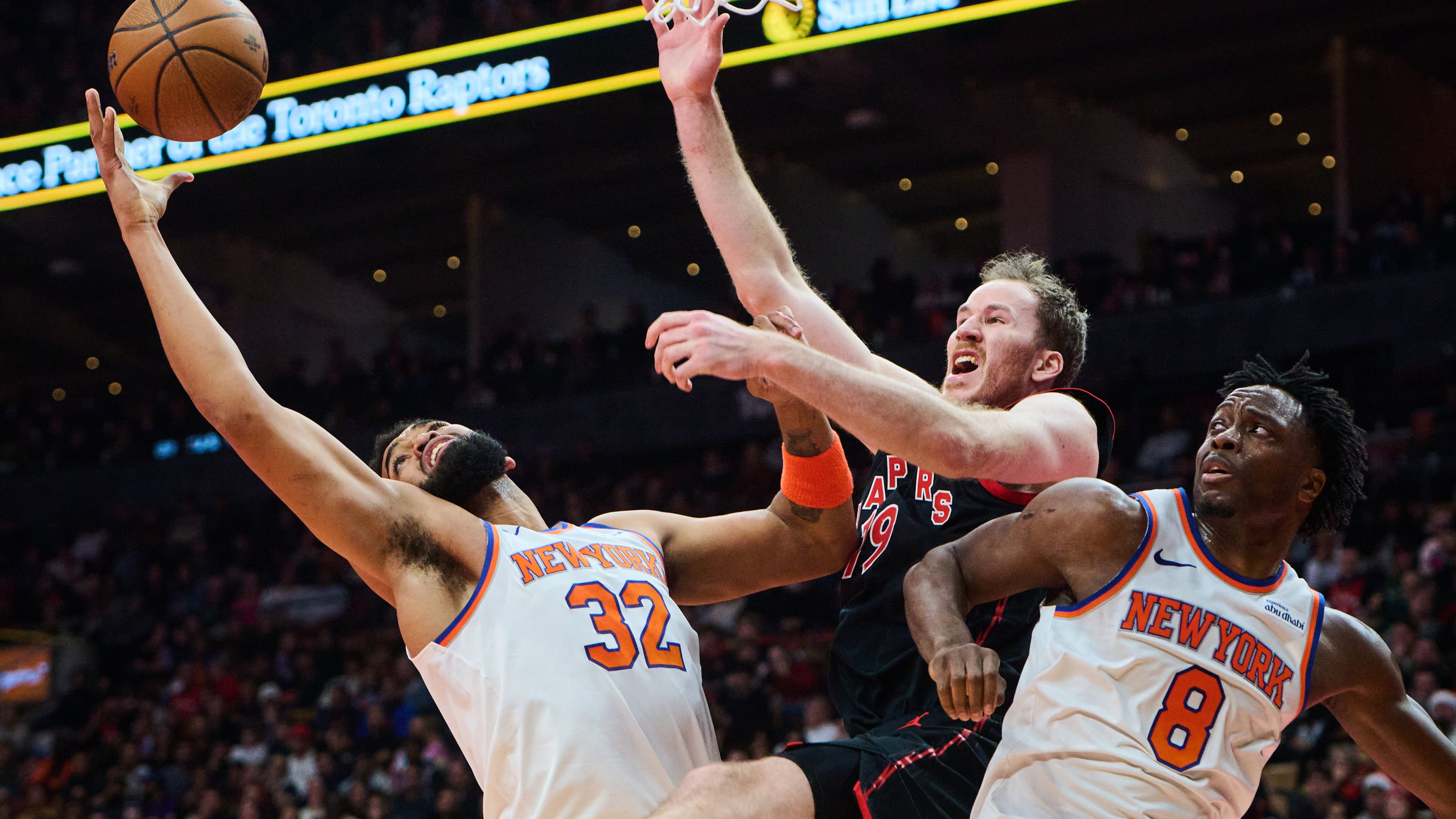 Toronto Raptors' Jakob Poeltl (19) is stopped at the net by New York Knicks' Karl-Anthony Towns (32) and New York Knicks' OG Anunoby (8) during the first half of an NBA Cup basketball game in Toronto, Tuesday, Dec. 9, 2025. (Sammy Kogan/The Canadian Press via AP)
