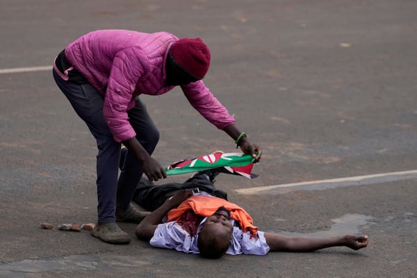 A protester covers a man with Kenyan flag, who the crowd claimed had been shot by police, during the historic 1990 Saba Saba, a Swahili word that means seven seven, protests for democratic reforms in the Kangemi slum of Nairobi, Kenya Monday, July 7, 2025. (AP Photo/Brian Inganga)