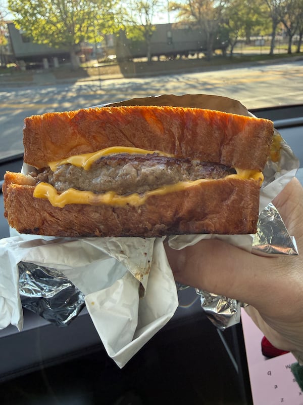 A hand holds a foil-wrapped burger: A large burger patty on thick-sliced grilled bread slices, with slices of cheese above and below the burger patty.