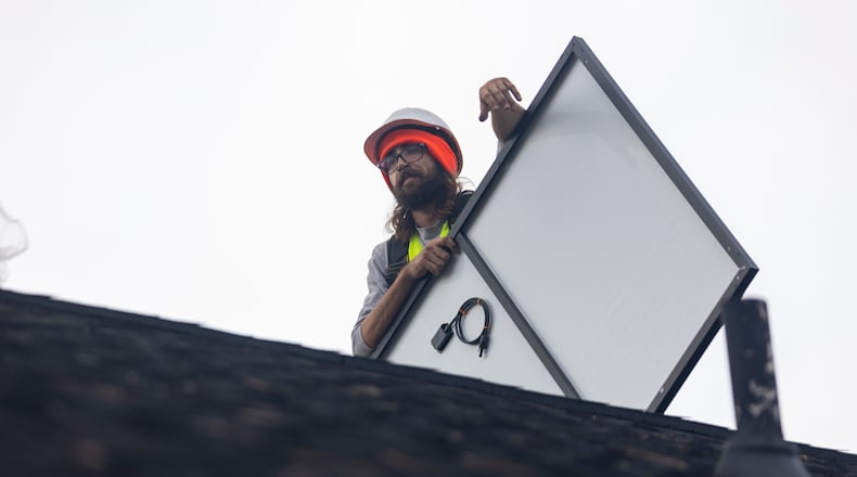 FILE: Joe McClain, an installer for Creative Solar USA, moves solar panels onto the roof of a home in Ball Ground, Georgia on Dec. 17th, 2021. (Nathan Posner for The Atlanta Journal-Constitution)