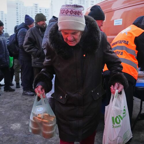 An elderly woman carries her bags out of a hot food distribution point during a power outage caused by Russia's repeated air strikes on the country's power grid, in Kyiv, Ukraine, Monday, Feb. 2, 2026. (AP Photo/Sergey Grits)