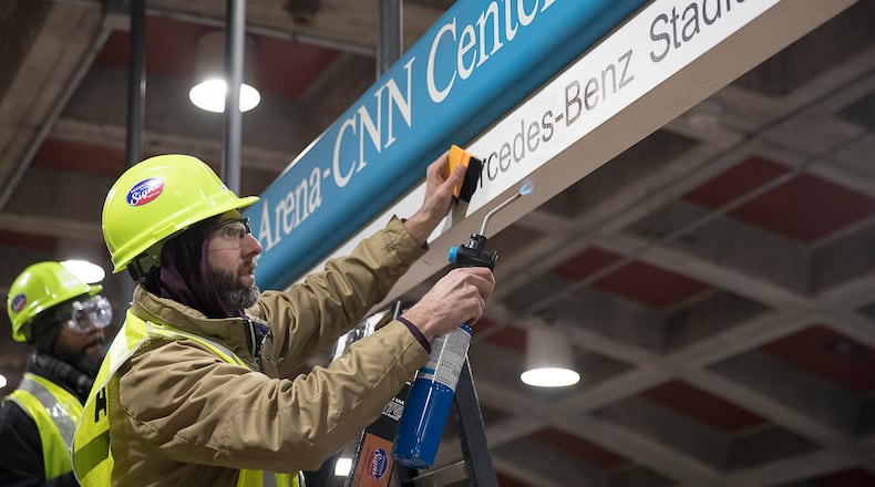 01/16/2019 -- Atlanta, Georgia -- Tim Carl (second from left) of Advantage Graphics & Signs uses a torch to gaurantee the cohesiveness of the new Mercedes-Benz signage at the MARTA Dome/GWCC/Philips Arena/CNN Center Transit in Atlanta, Wednesday, January 16, 2019. Advantage Graphics & Signs worked in the transit station on Wednesday to replace signage that mislabeled Atlanta's two newly named sport stadiums. (ALYSSA POINTER/ALYSSA.POINTER@AJC.COM)