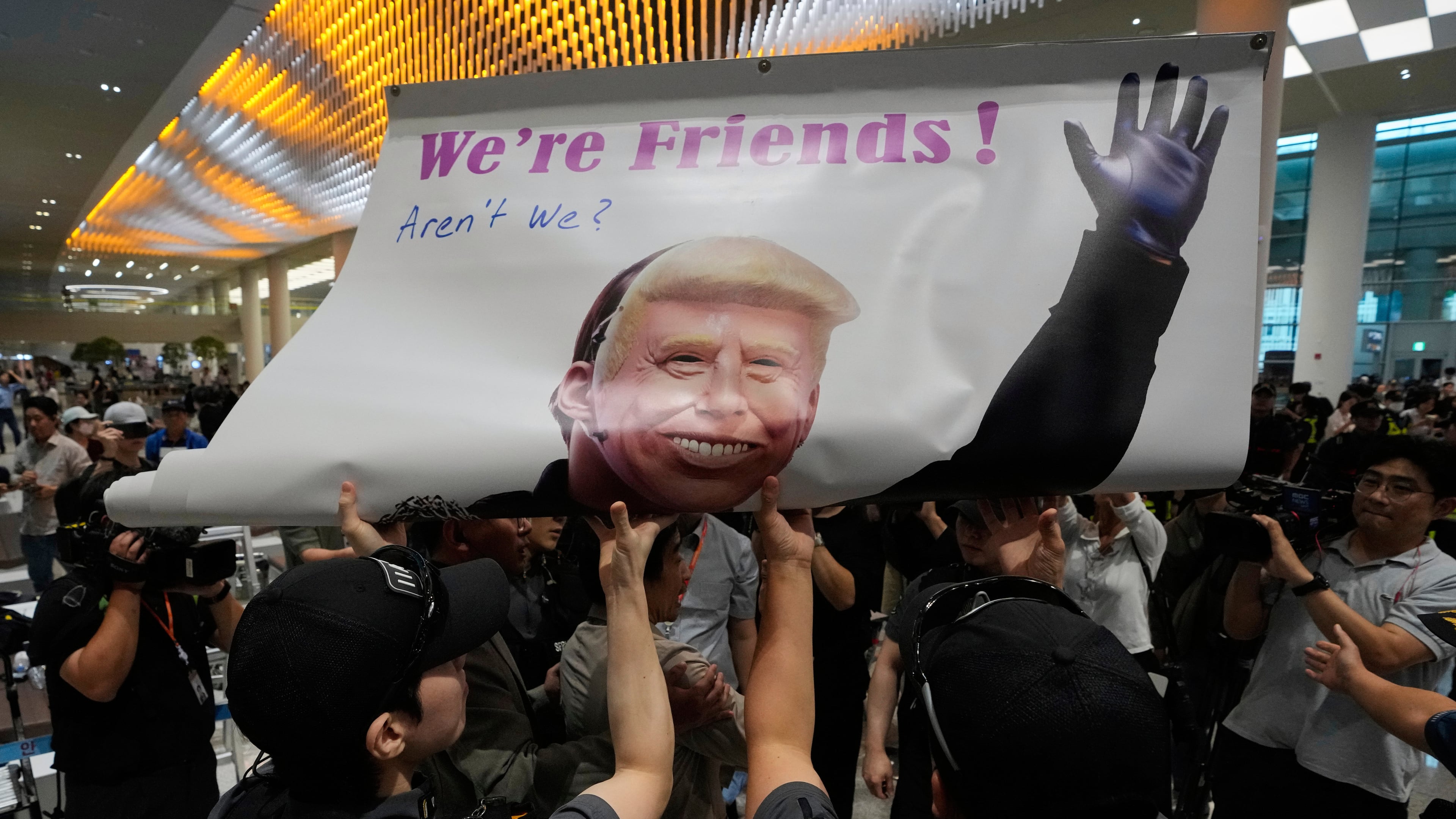 Protesters try to hold a banner depicting U.S. President Donald Trump as police officers and members of airport security block at the arrival terminal of the Incheon International Airport, in Incheon, South Korea, Friday, Sept. 12, 2025. (Ahn Young-joon/AP)