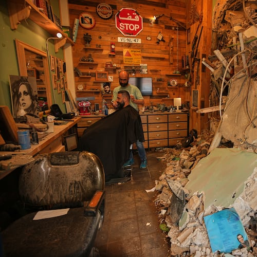 Barber Mohammad Mehdi cuts the hair of his client Ayman Al Zein inside his shop, which was damaged in an Israeli airstrike that also damaged Al Zein's shop, in Dahiyeh, Beirut's southern suburbs, Lebanon, Saturday, April 18, 2026. (AP Photo/Hassan Ammar)