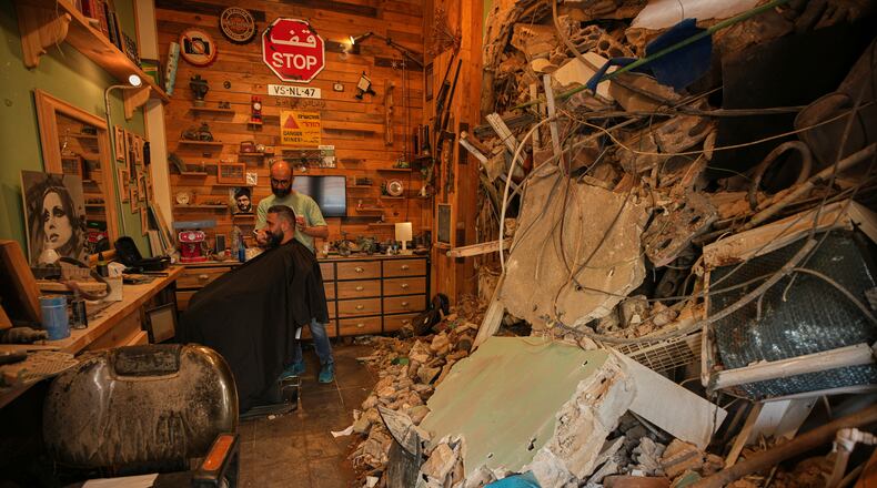 Barber Mohammad Mehdi cuts the hair of his client Ayman Al Zein inside his shop, which was damaged in an Israeli airstrike that also damaged Al Zein's shop, in Dahiyeh, Beirut's southern suburbs, Lebanon, Saturday, April 18, 2026. (AP Photo/Hassan Ammar)
