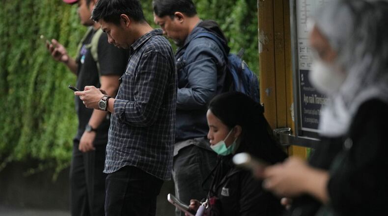 People use their mobile phones at a bus stop in Jakarta, Indonesia, Friday, March 6, 2026. (AP Photo/Dita Alangkara)