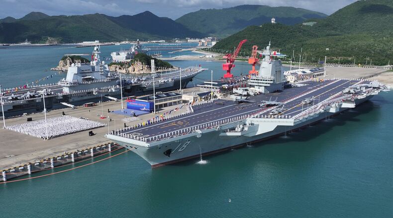 In this photo released by Xinhua News Agency, a commissioning and flag-presenting ceremony of the Fujian, China's third aircraft carrier and the first that it has both designed and built itself equipped with electromagnetic catapults, seen on right at a naval port in Sanya city in southern China's Hainan Province, on Wednesday, Nov. 5, 2025. (Li Gang/Xinhua via AP)