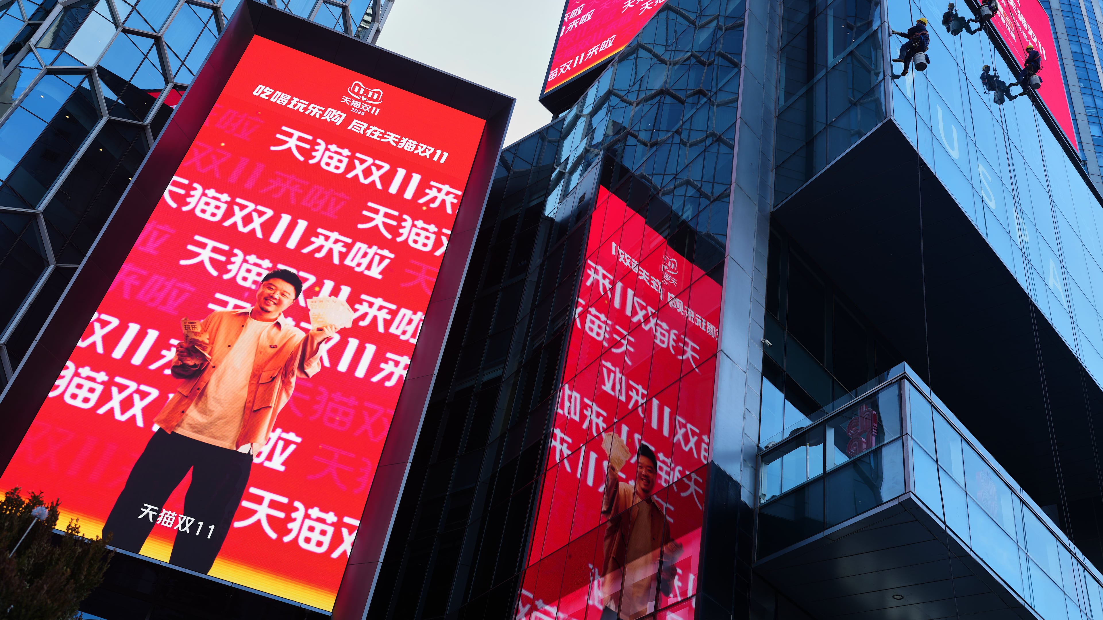 Window cleaners labor an commercial office as an advertisement billboard promoting Tmall's Singles' Day sale at a shopping district in Beijing on Nov. 10, 2025. (AP Photo/Andy Wong)