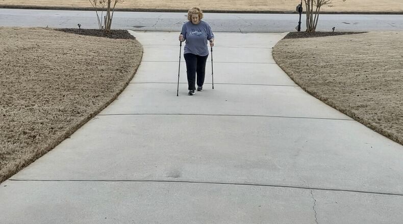 Stephanie Schroeder of McDonough taking a walk up her driveway. Because long COVID has wreaked havoc with her balance, she says she uses the walking sticks to steady herself. “Some days, I’m all right, but I can’t tell you which days I will feel good,” she said. “It’s all very frustrating because you know what you were capable of doing before.” (Contributed)