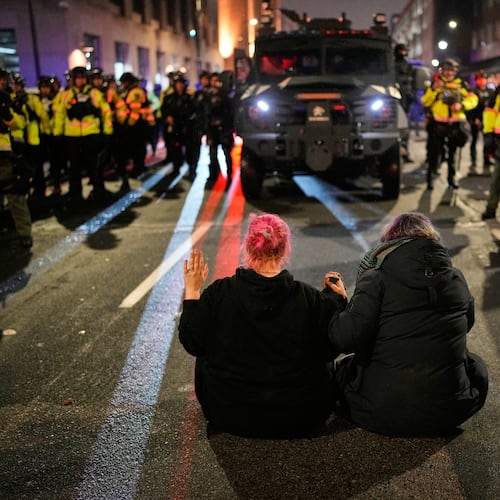 Two people sit in the street holding hands in front of Minnesota State Patrol during a protest and noise demonstration calling for an end to federal immigration enforcement operations in the city, Friday, Jan. 9, 2026, in Minneapolis. (AP Photo/John Locher)