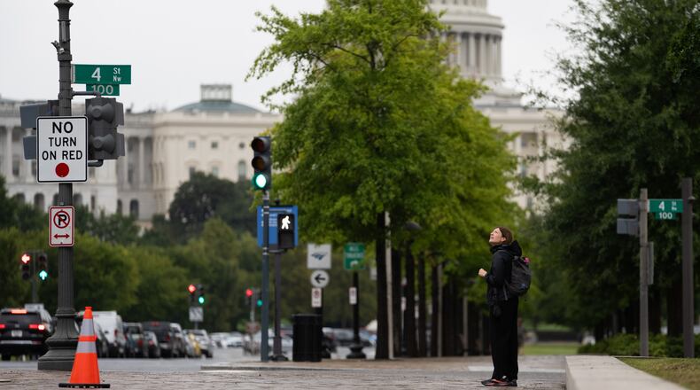 An individual watches a protester scale a light pole and unfurl a banner to protest the upcoming State Visit by China's President Xi Jinping, Tuesday, Sept. 22, 2026, in Washington. (AP Photo/Allison Robbert)