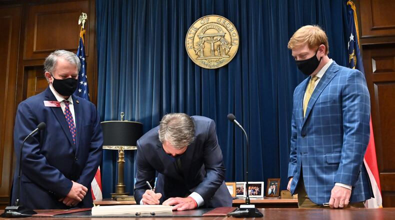 Gov. Brian Kemp signs the fiscal 2021 budget as House Appropriations Chairman Terry England (left) and Senate Appropriations Chairman Blake Tillery look on. (Hyosub Shin / Hyosub.Shin@ajc.com)