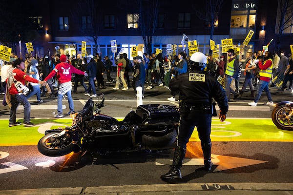 An Atlanta police officer stands by his downed motorcycle as protestors march against Immigration and Customs Enforcement in Atlanta on Thursday, Jan. 8, 2026, the day after Renee Good was shot and killed by an ICE agent in Minneapolis. (Arvin Temkar/AJC)